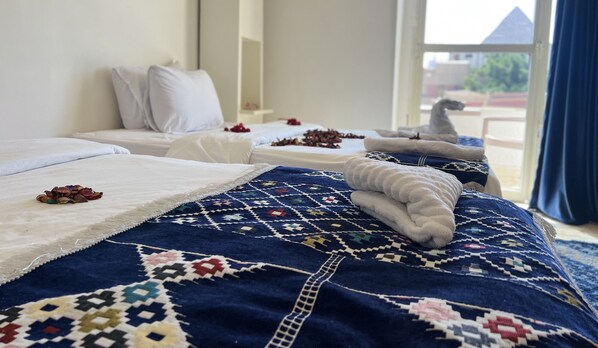 A hotel room with two beds, each with a white comforter and a blue patterned blanket. There are decorative pillows and a small pile of dried flowers on one bed. - Pyramids Top Inn (Giza)