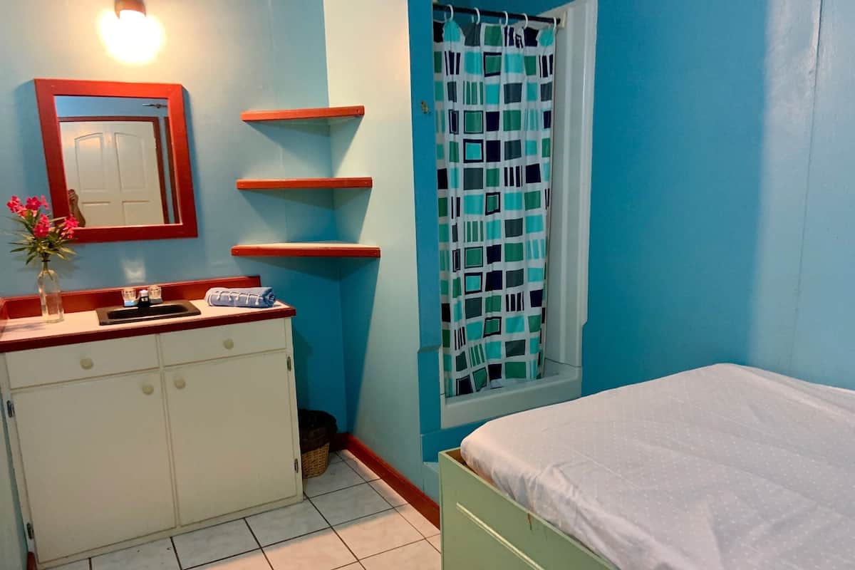 A bedroom with a bed, a dresser, a mirror, and a window with a curtain.