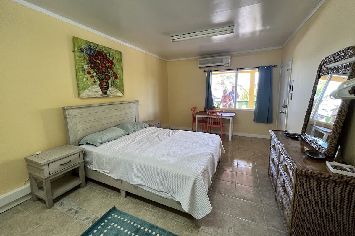 A bedroom with a bed, a desk, a chair, a dresser, and a painting on the wall.