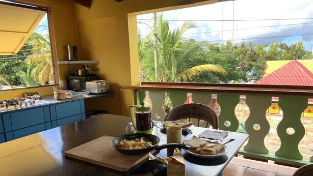 A kitchen with a dining area, a view of the outdoors, and a table with food and utensils. - The Waterfront Inn - Hostel (English Harbour)