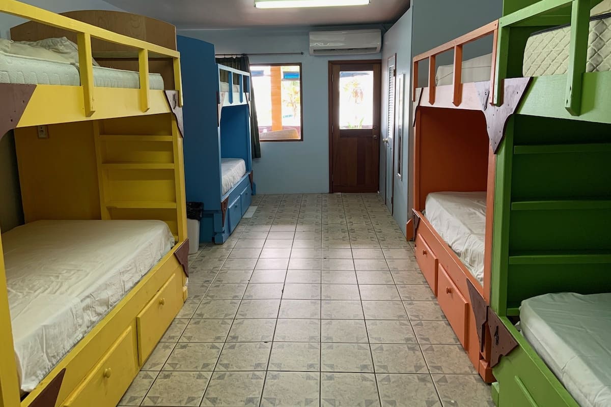 A dormitory room with bunk beds, a tiled floor, and a door leading to another room.