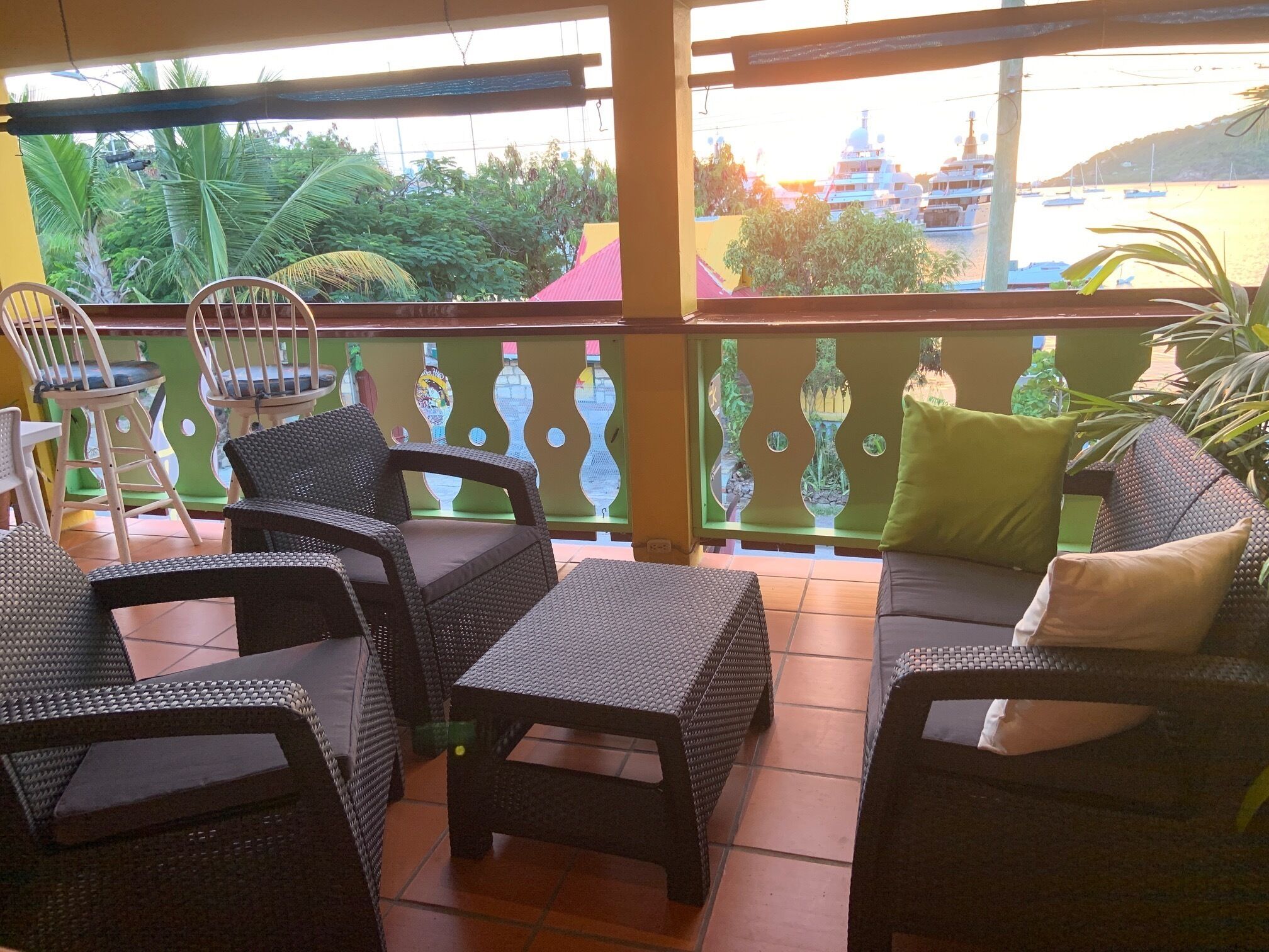 A covered outdoor seating area with wicker furniture, a decorative fence, and a view of a beach and buildings in the distance.