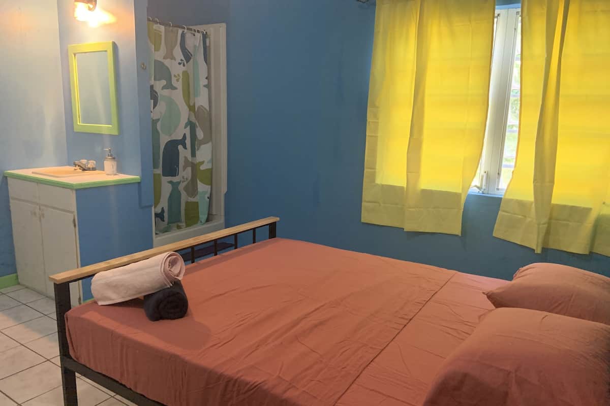 A bedroom with a bed, a bedside table, a mirror, and a window with curtains.