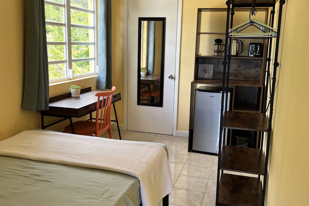 A compact hotel room with a bed, a desk, a small kitchenette, and a bathroom.
