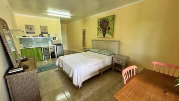 A hotel room with a bed, a desk, a chair, a small table, a mirror, a green curtain, and a painting on the wall.