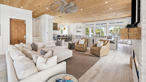 A spacious living area with a wooden ceiling, a large sofa, armchairs, and a dining area with pendant lights. - Seas Above the Rest - Short Walk to the Beach! Large Resort Style Private Pool! (Destin)