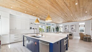 A modern kitchen with a central island, white cabinets, and a wooden ceiling. - Seas Above the Rest - Short Walk to the Beach! Large Resort Style Private Pool! (Destin)