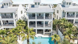 A multi-story hotel with balconies, a swimming pool, and palm trees. - Seas Above the Rest - Short Walk to the Beach! Large Resort Style Private Pool! (Destin)