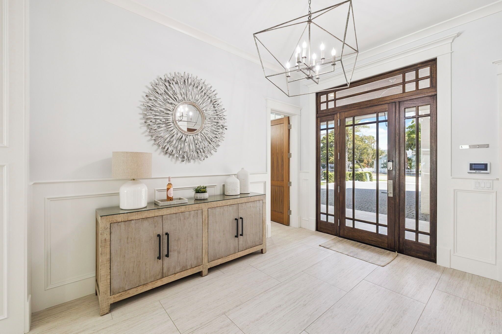 A spacious foyer with a wooden cabinet, a decorative mirror, and a geometric chandelier.