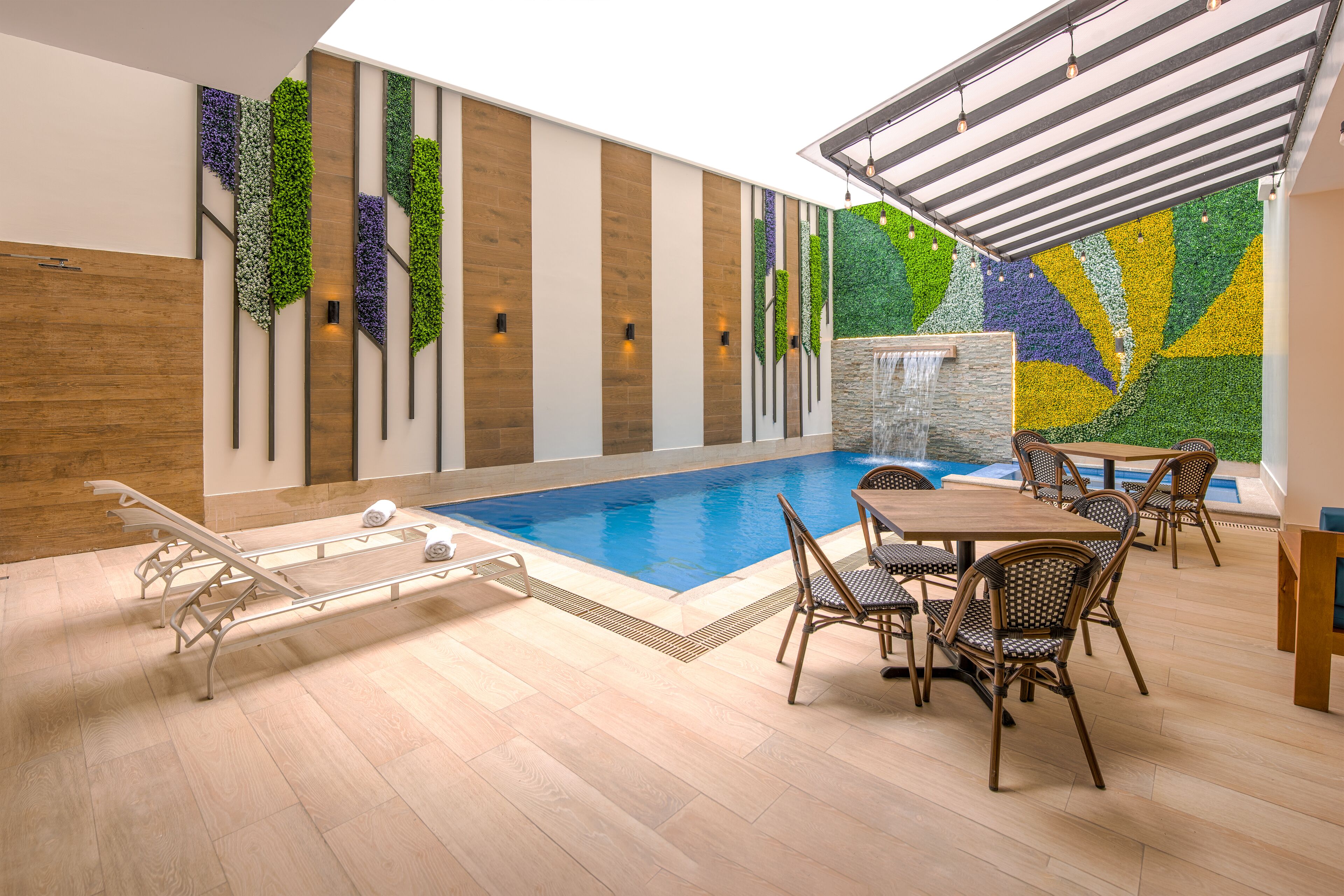 Un espace piscine doté d’une terrasse en bois, de chaises longues et d’une table à manger avec des chaises.