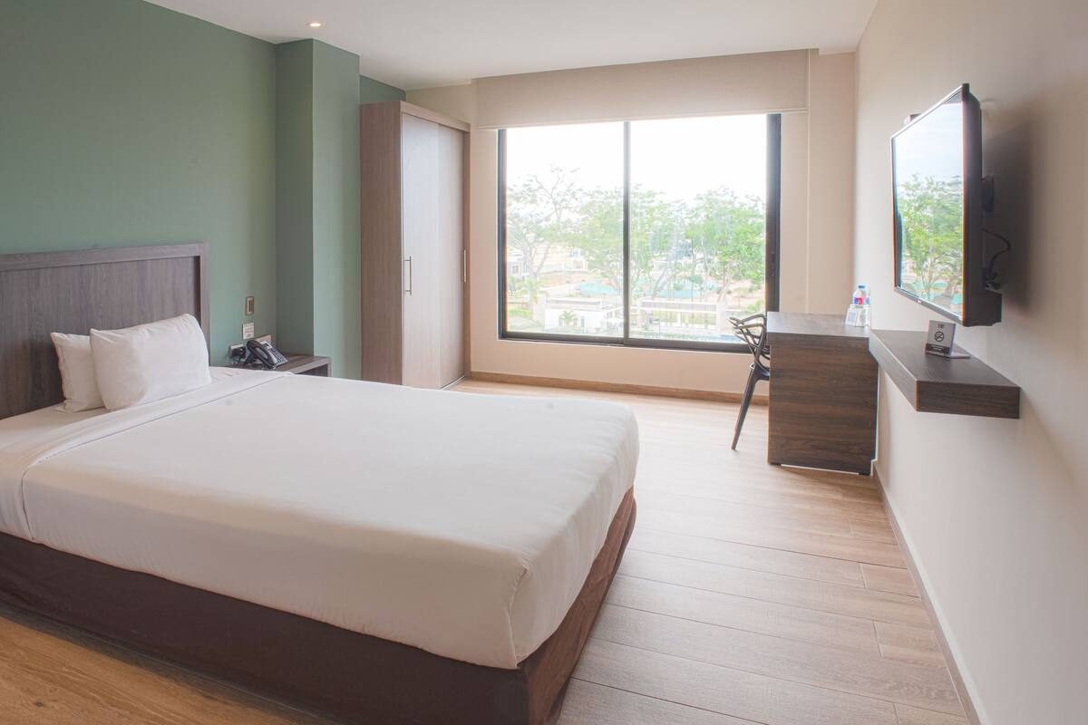 A hotel room with a large bed, a desk, a chair, a TV, and a window with a view of the outdoors.