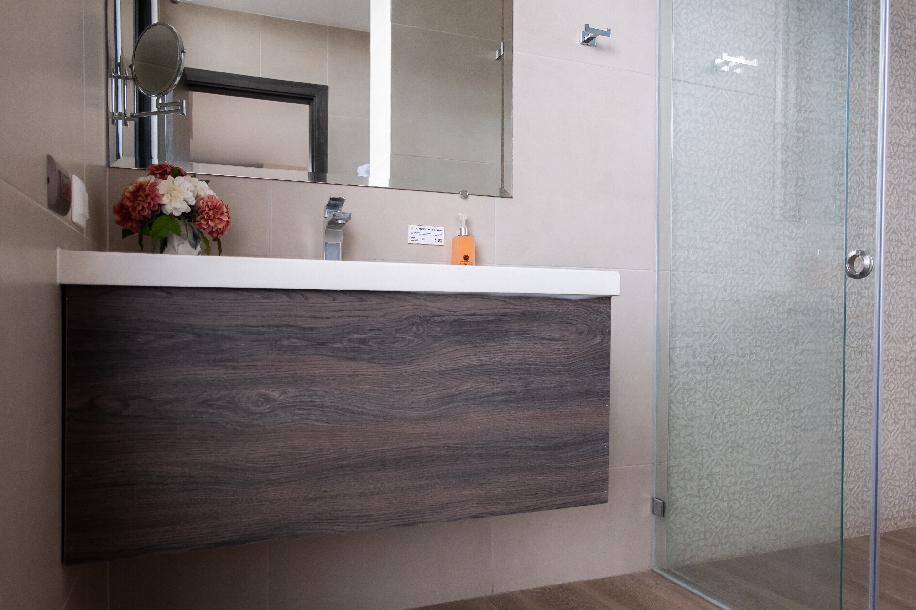 Un baño con tocador de madera oscura, espejo, florero y cabina de ducha de vidrio.