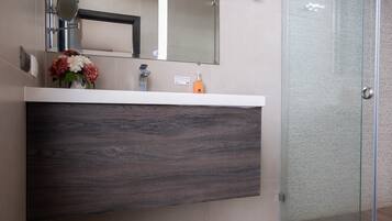 Un baño con tocador de madera oscura, espejo, florero y cabina de ducha de vidrio.