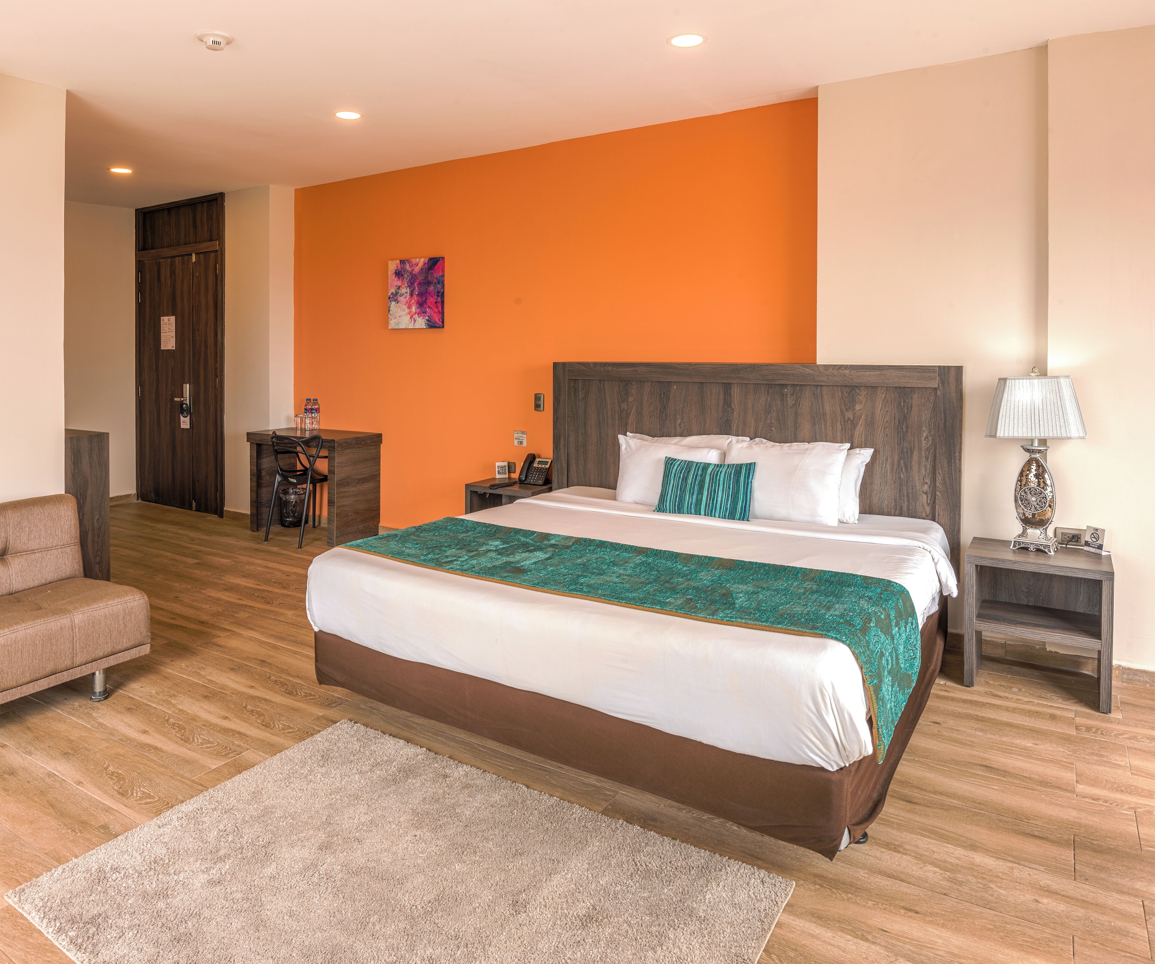 Una habitación de hotel con una cama grande, un cabecero de madera, un escritorio con una silla, una mesita con una lámpara y un sofá.