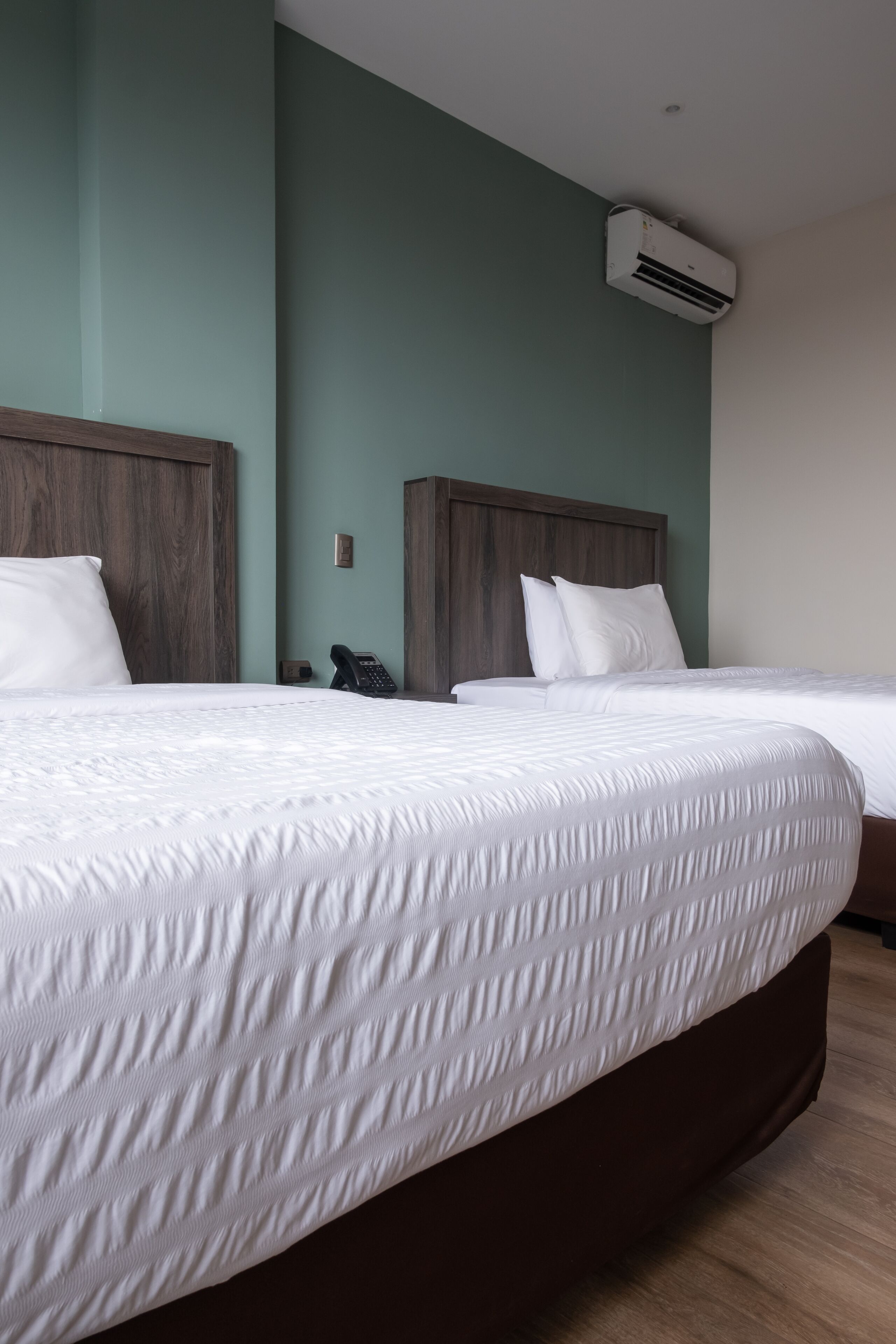 A hotel room with two beds, a wooden headboard, a phone, and an air conditioning unit.