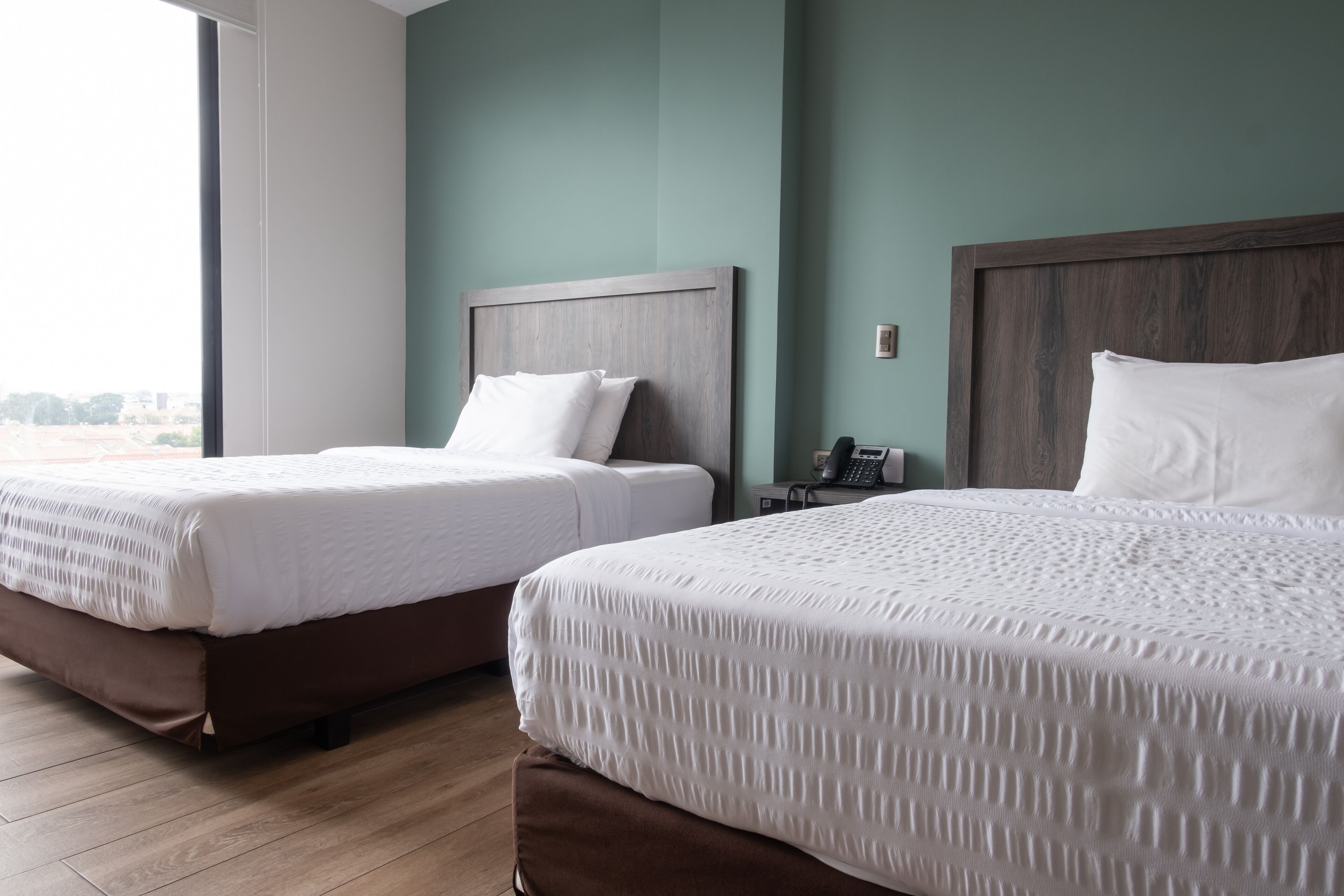 Dos camas individuales con cabeceros de madera en una habitación con paredes verde azulado y suelo de madera.