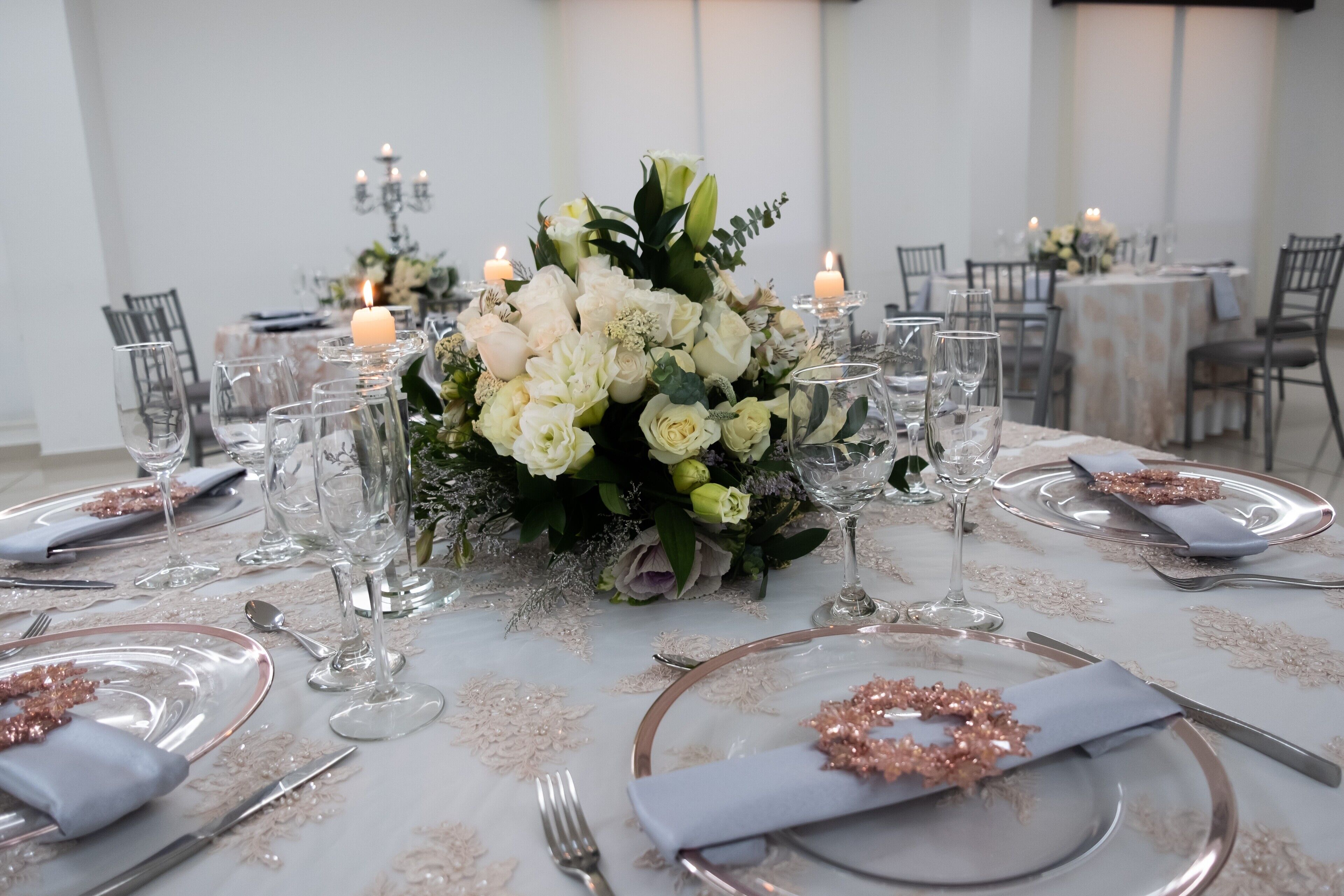 A formal dining table set with white tablecloth, silverware, and glassware, surrounded by candles and a floral centerpiece.
