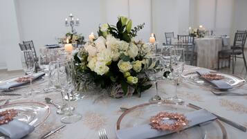 Mesa formal para comedor con mantel blanco, cubertería y cristalería, rodeada de velas y un centro de mesa floral.