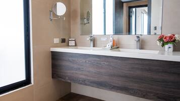 Un baño moderno con un espejo grande, tocador con encimera de madera oscura y un jarrón con flores.