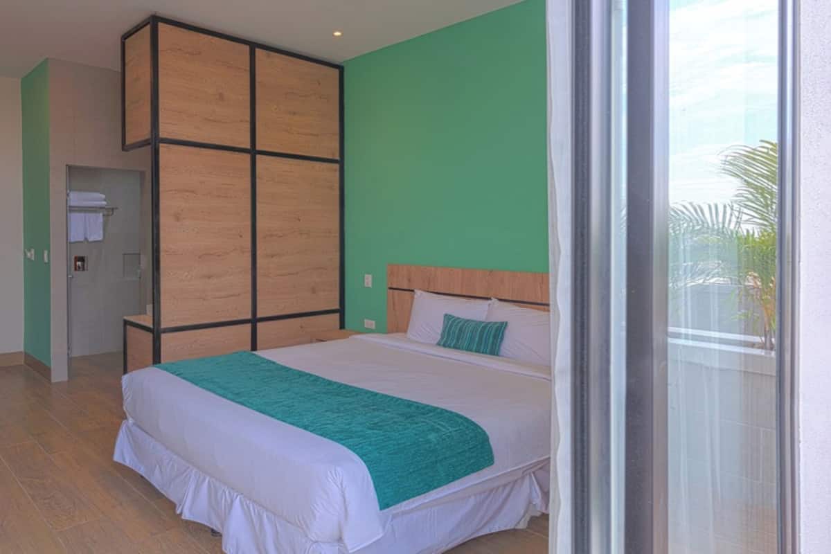 A bedroom with a large bed, a wooden wardrobe, and a view of greenery outside.