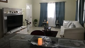 Ein Wohnzimmer mit Fernseher, einer Couch, einem Esstisch mit Kerze und einem Deckenventilator.