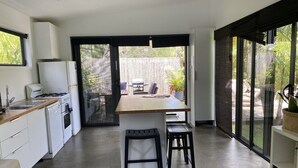 A modern kitchen with a central island, bar stools, and a view of the outdoor patio area. - Bali in Berrara (Berrara)