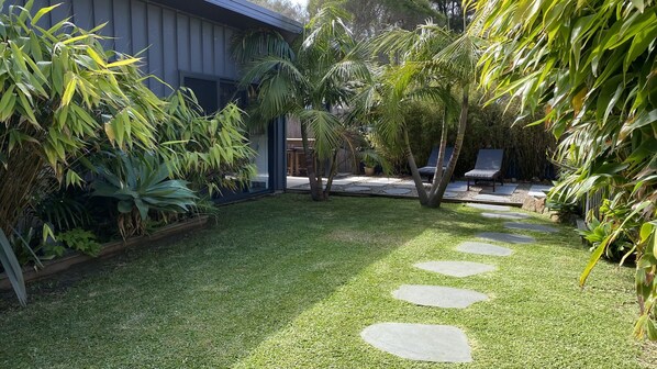 Un jardín cuidado con césped, piedras para caminar y una variedad de plantas tropicales.