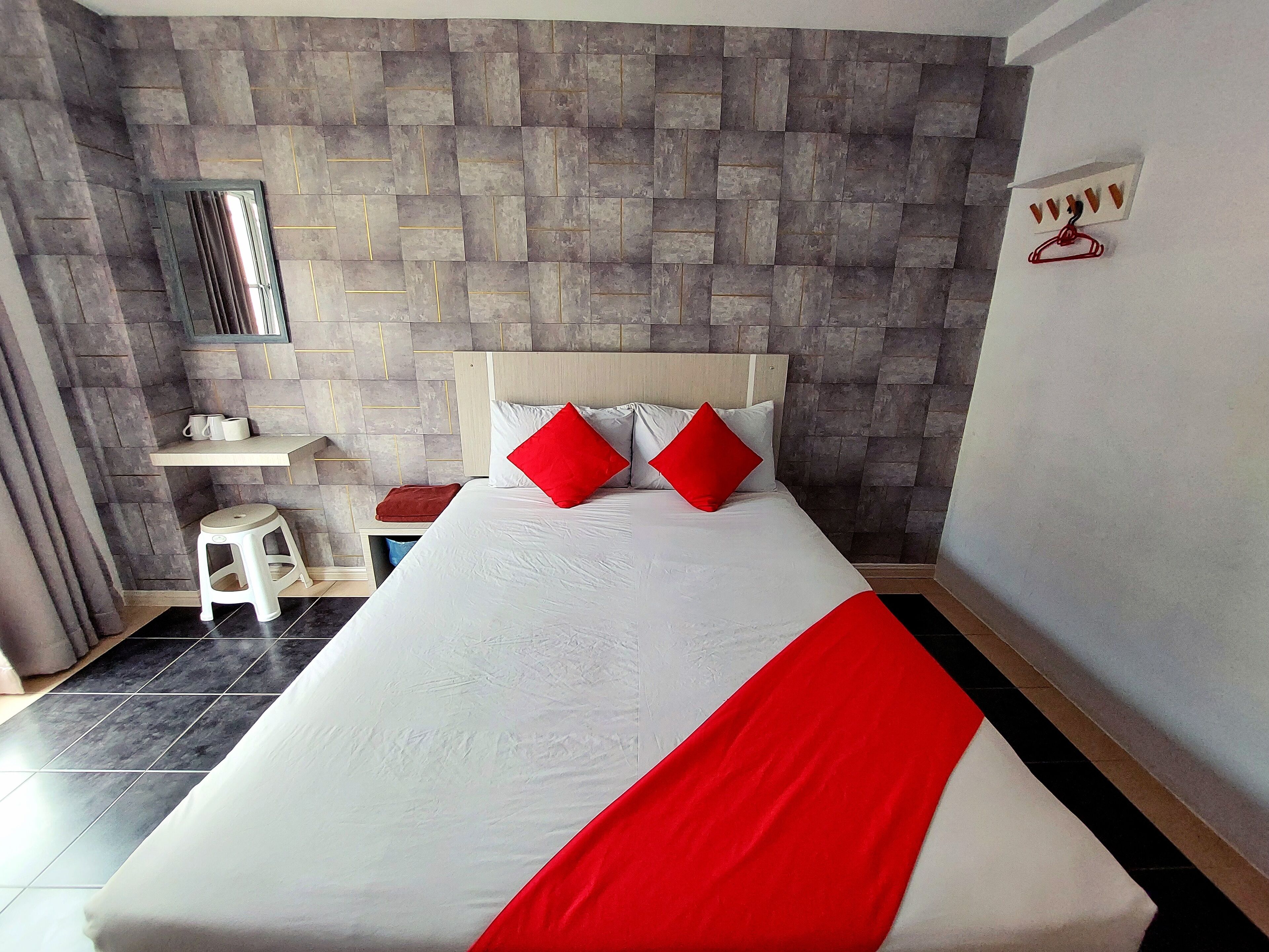 Habitación de hotel con una cama grande, una mesita de noche, un espejo y un perchero en la pared.