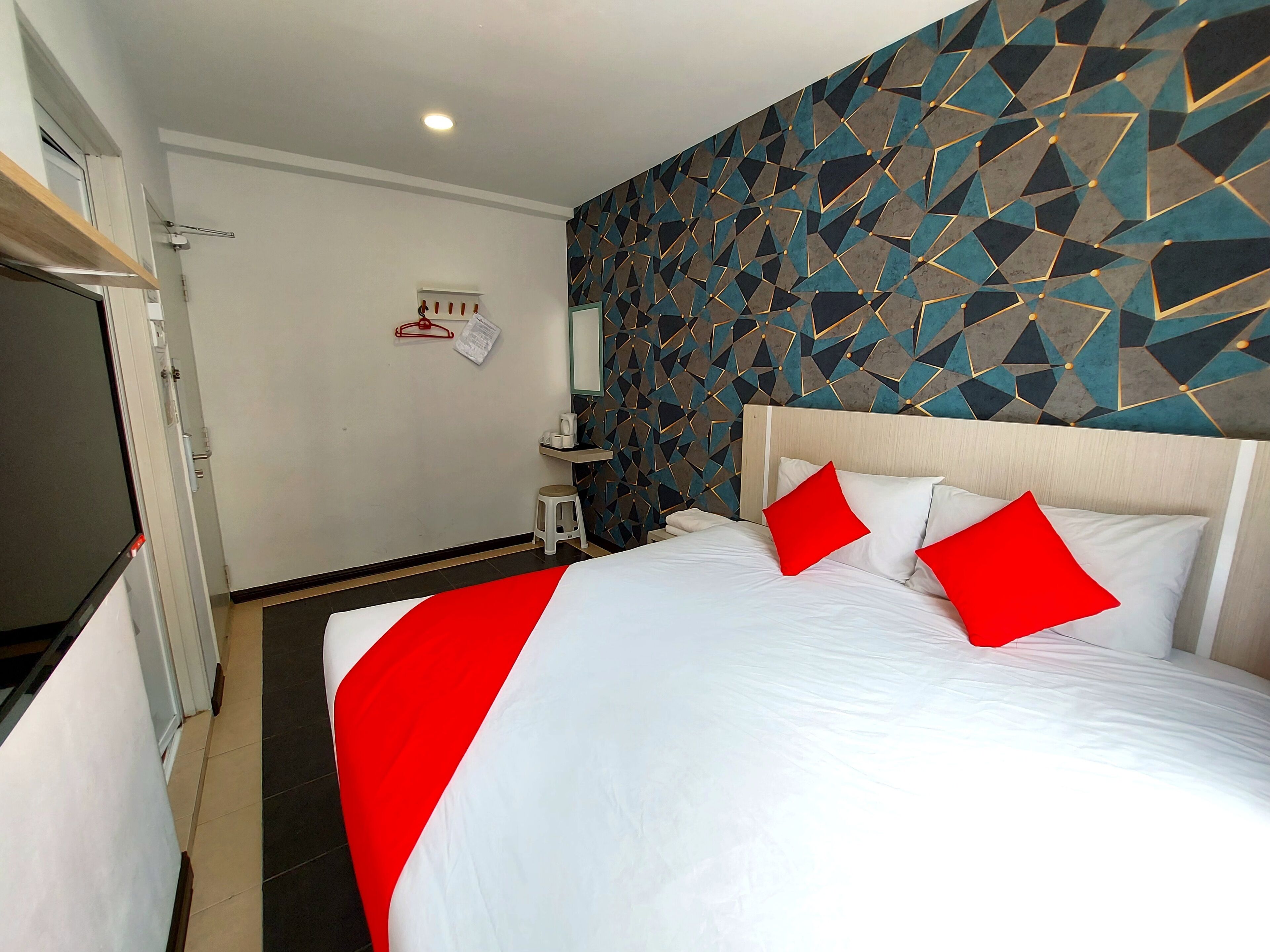Habitación de hotel con una cama grande, un papel tapiz con diseño geométrico, un taburete pequeño y un estante con artículos de aseo.