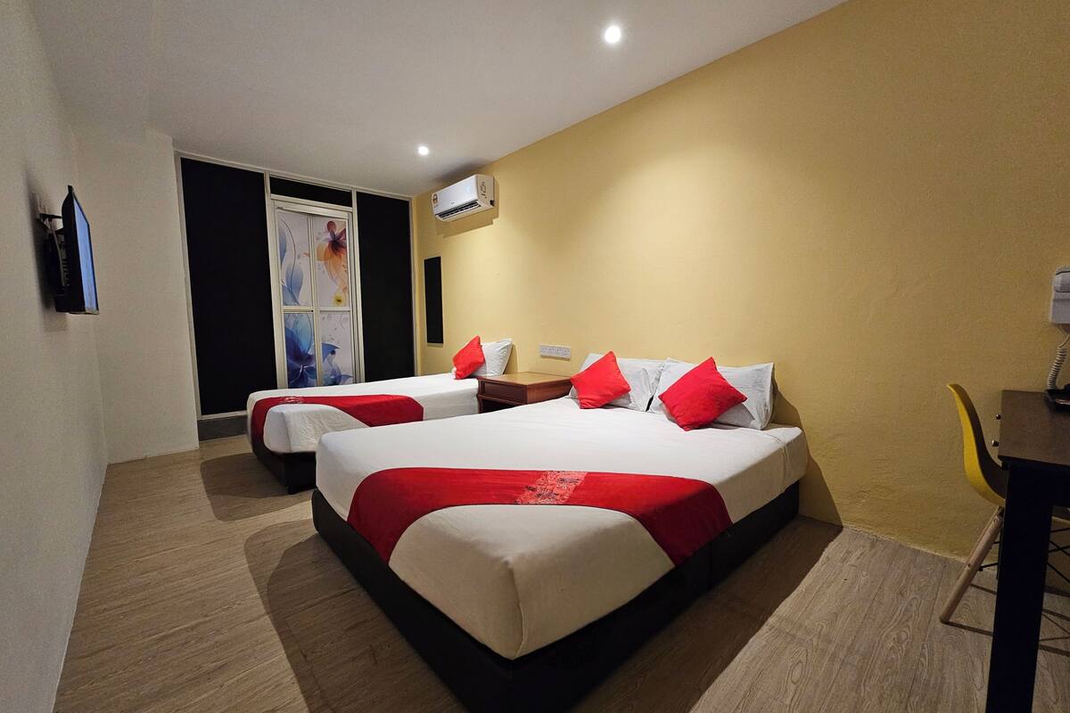 A hotel room with two beds, a desk, an air conditioning unit, and a wall-mounted TV.