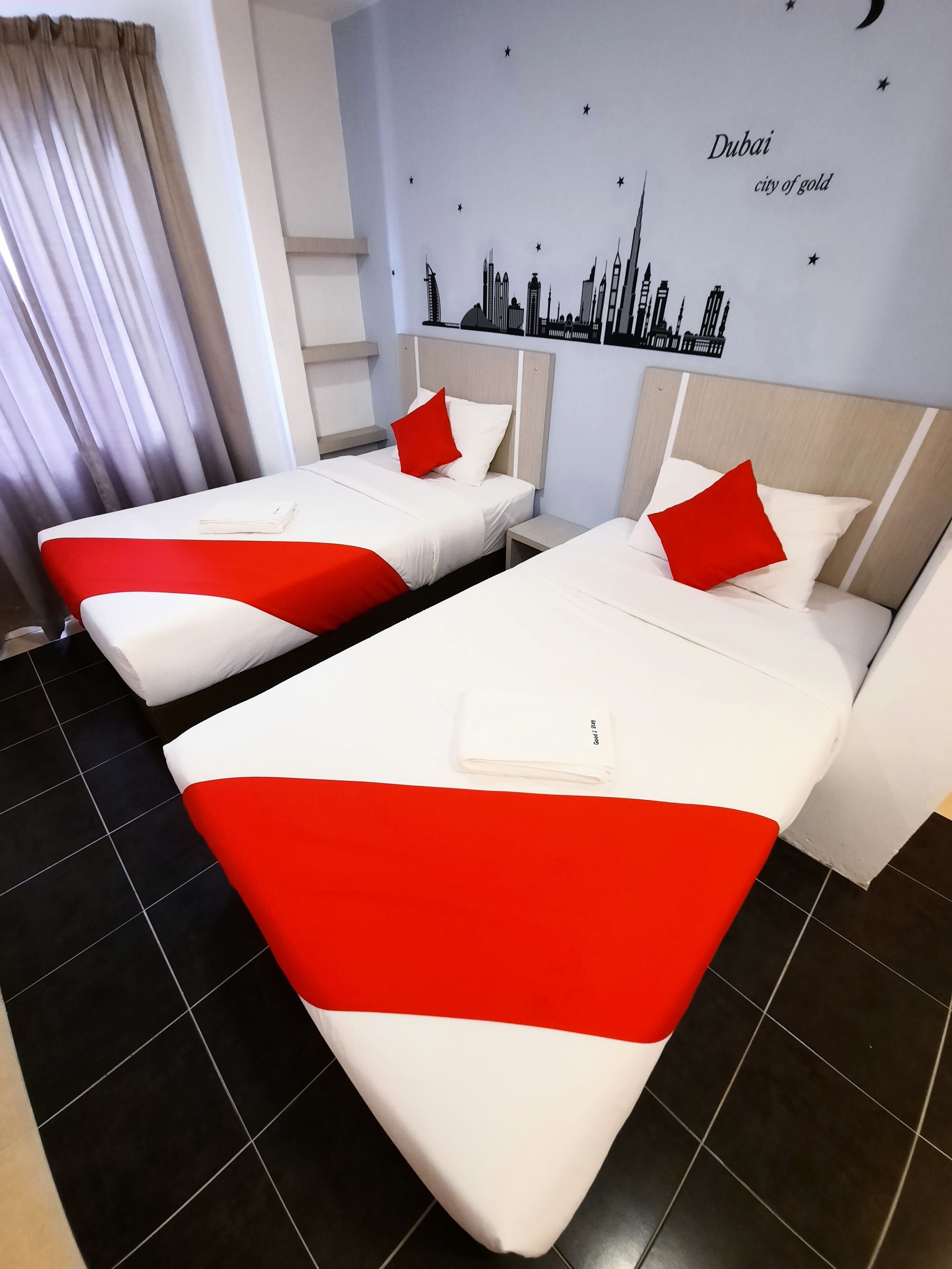 Zwei Betten mit rot-weißer Bettwäsche, eine Stadtlandschaft als Wandbild und ein Vorhang.