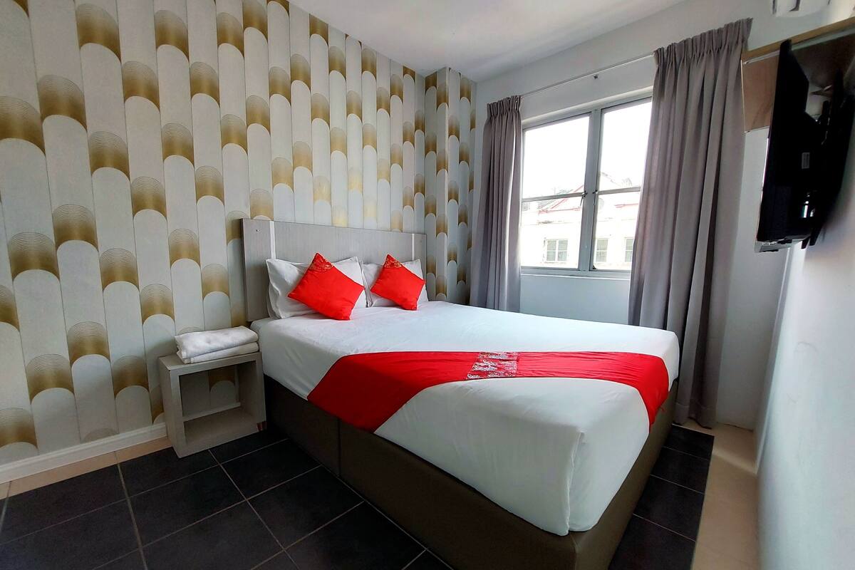 A hotel room with a large bed, a nightstand, a TV, and a window with curtains.