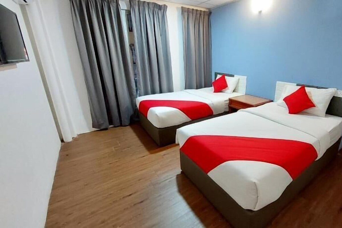 Two single beds with red and white bedding, grey curtains, and a wooden floor in a room with blue walls.