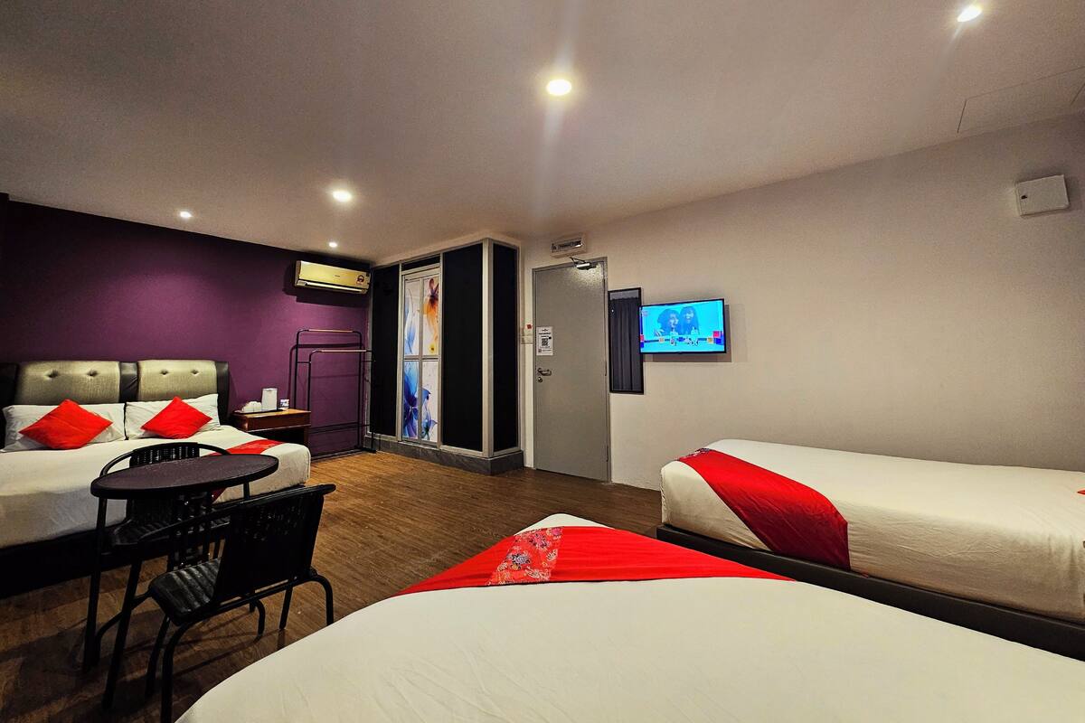 A hotel room with two beds, a small table, a chair, a TV, and an air conditioning unit.