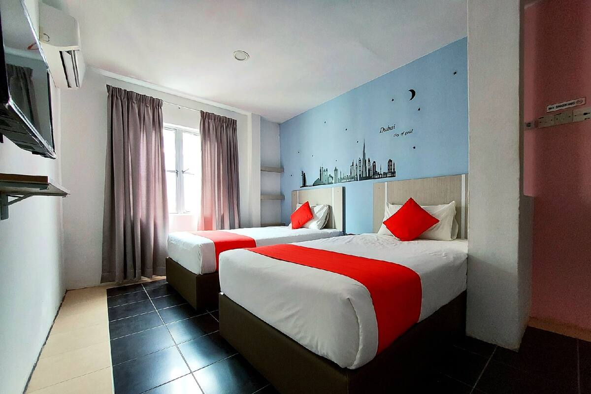 A hotel room with two beds, a city skyline mural, a window with curtains, and a tiled floor.