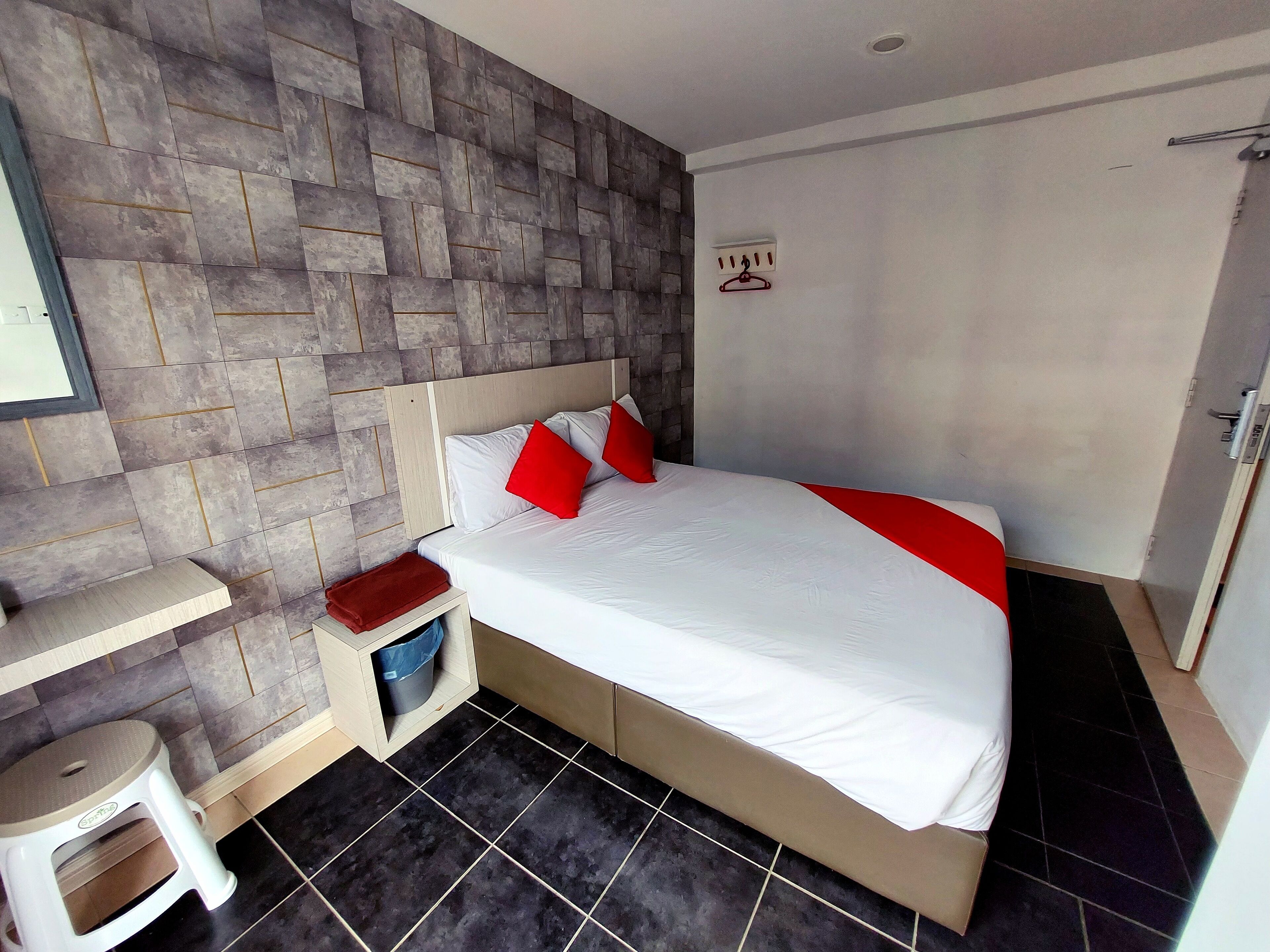 Une chambre d’hôtel avec un lit, une table de chevet, une serviette rouge, un petit tabouret et un mur dont le motif ressemble à de la pierre.