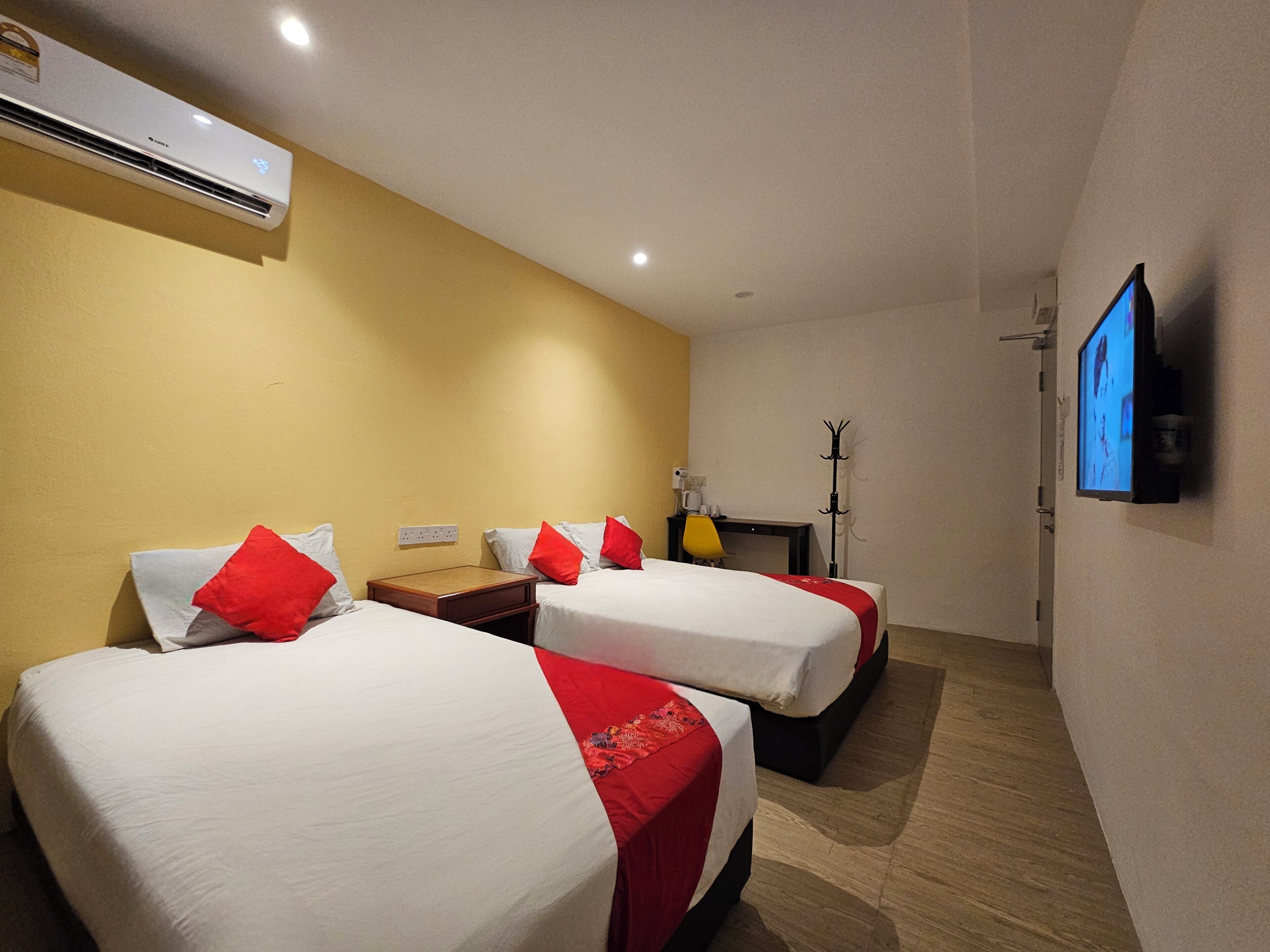 Une chambre d’hôtel avec deux lits, une télévision, un climatiseur et un bureau avec une chaise.