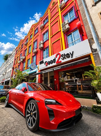 A red sports car parked in front of a brightly colored hotel with a sign reading 'Good2Stay.'. Good2Stay Hotel
