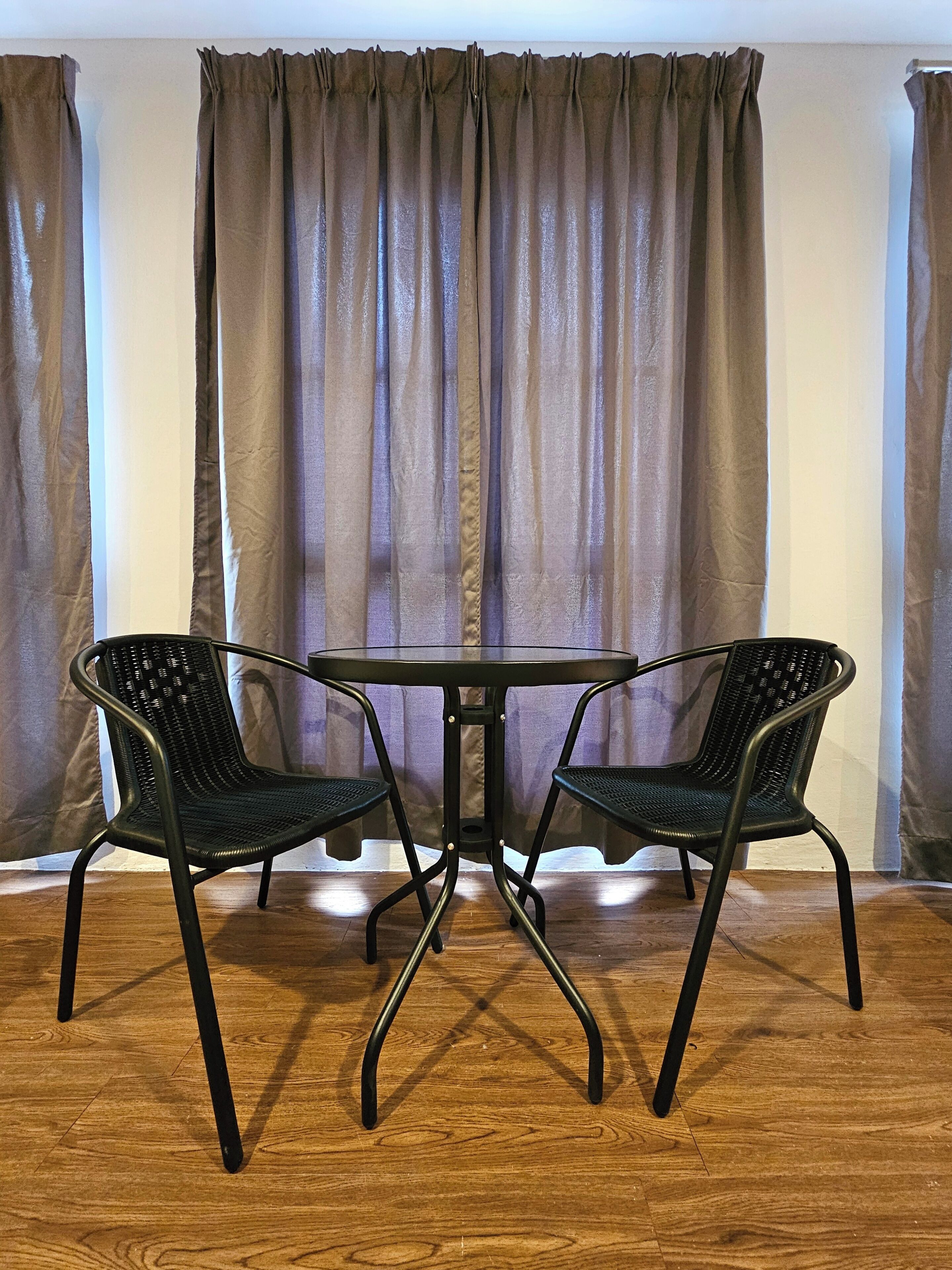 A room with a round table and two chairs, a wooden floor, and curtains.