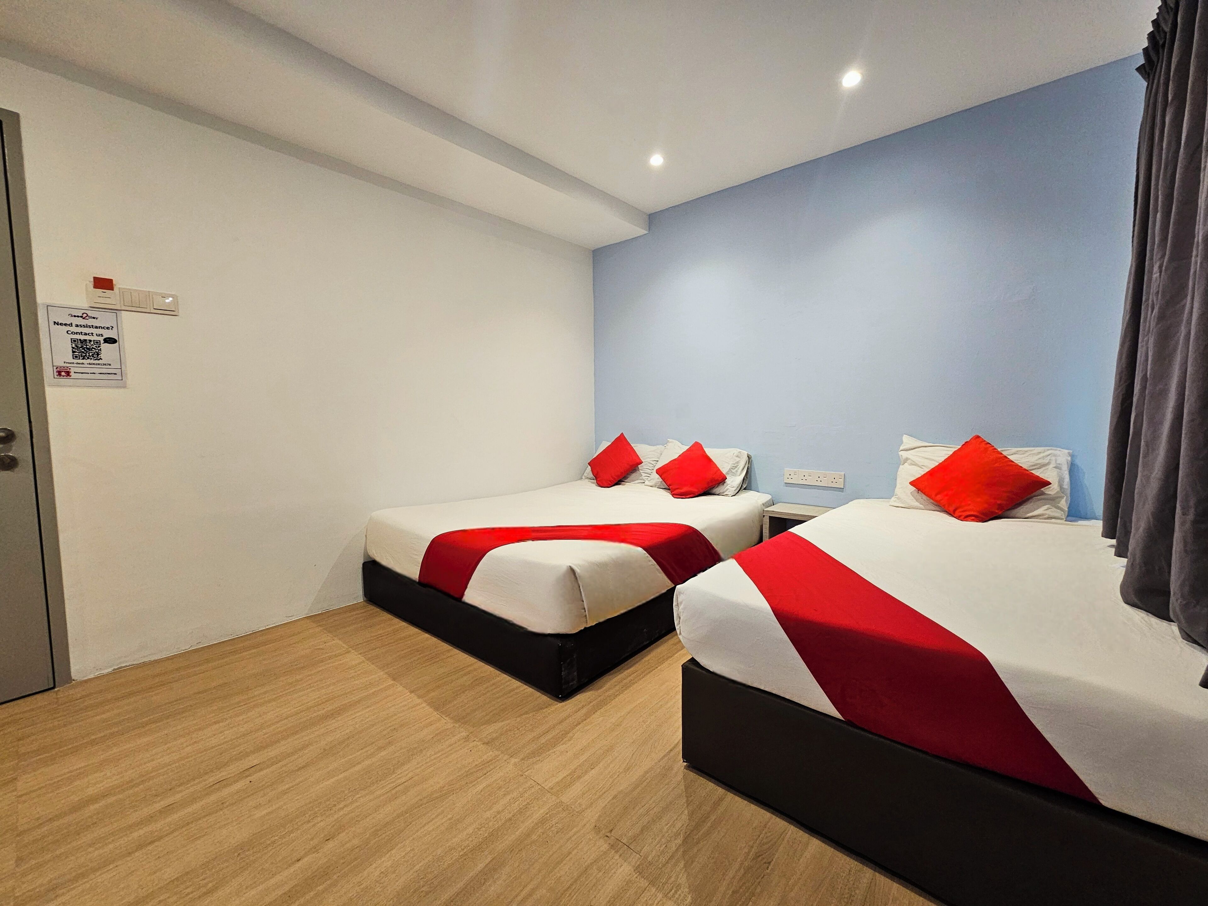 Habitación de hotel con dos camas, piso de madera, pared azul de acento y una puerta con un aviso.