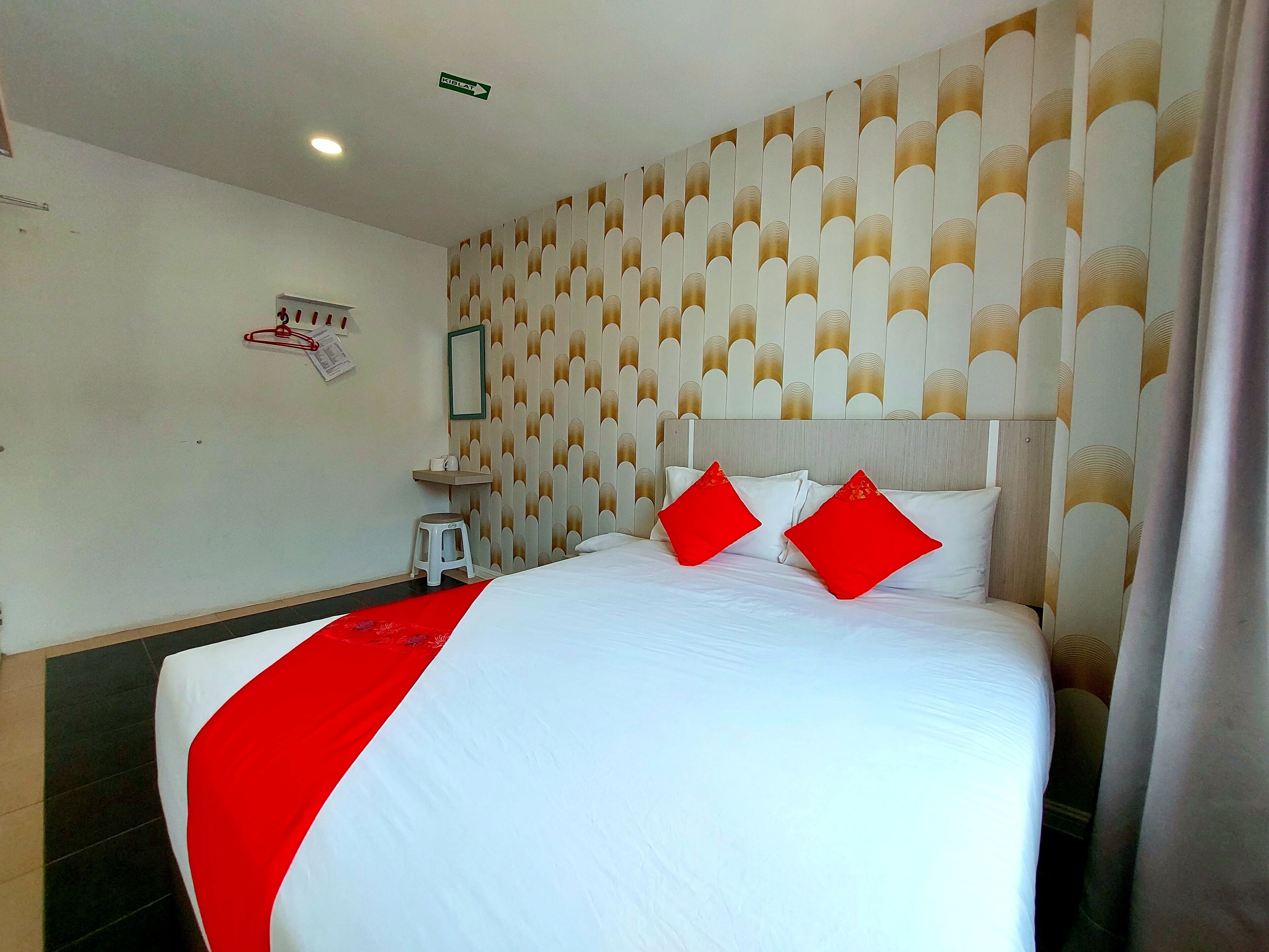 A hotel room with a large bed, a small stool, a wall-mounted shelf, and a patterned wallpaper.