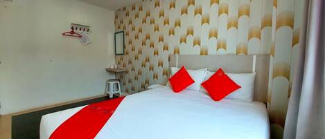 A hotel room with a large bed, a small stool, a wall-mounted shelf, and a patterned wallpaper.