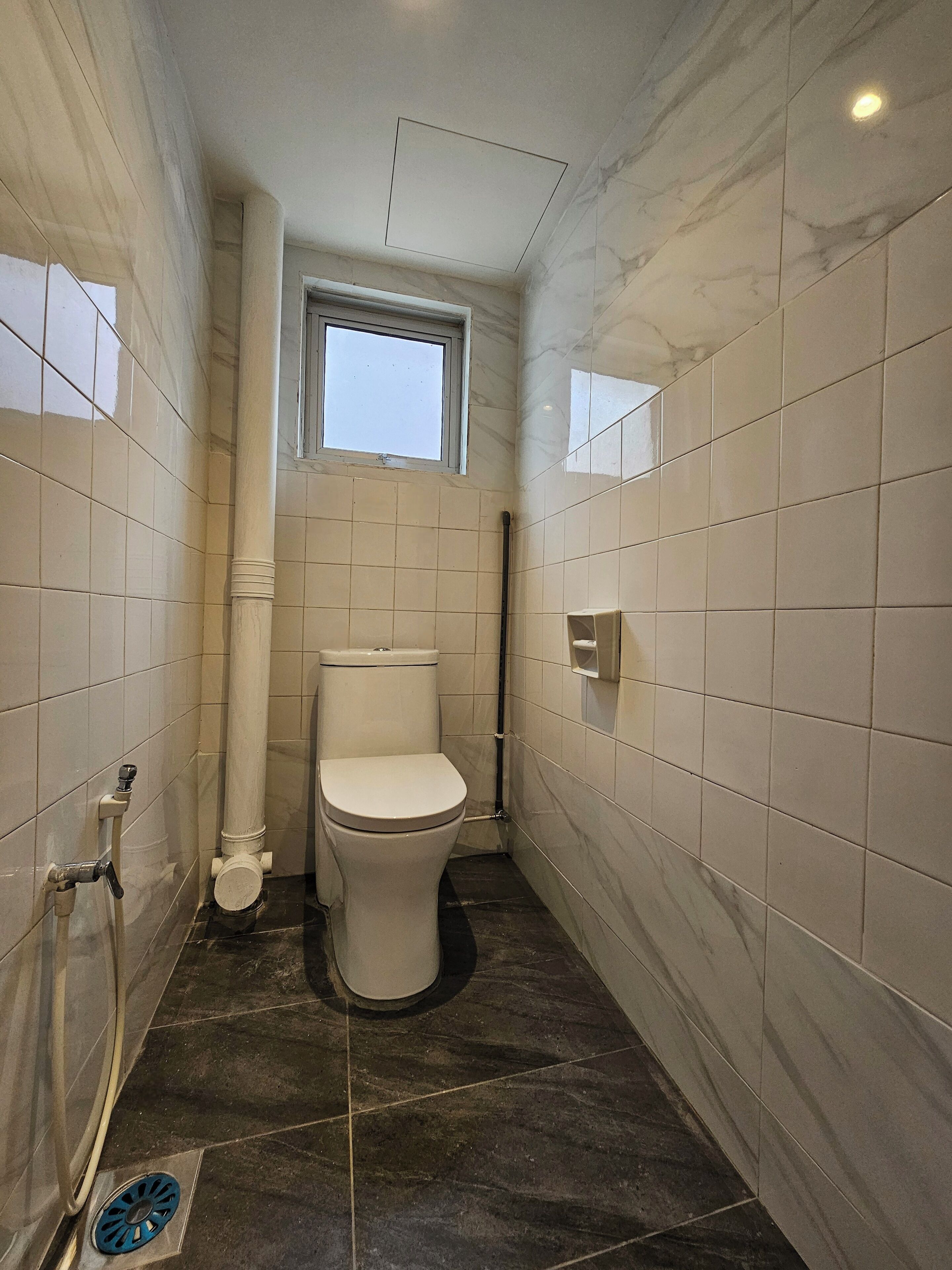 Ein kleines, schmales Badezimmer mit Toilette, Fenster und Fliesenwänden.