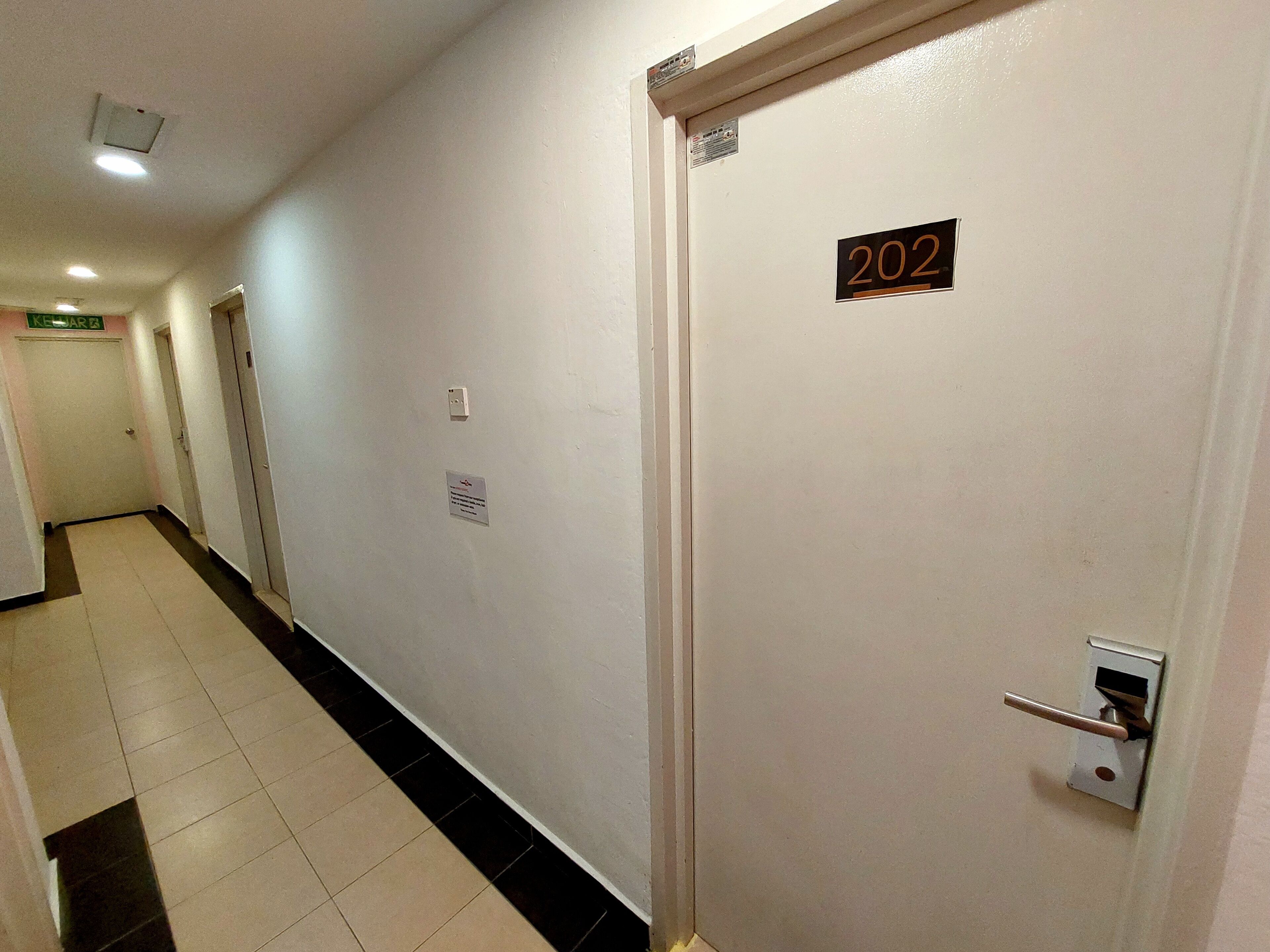 Un passadís amb una porta etiquetada com a 202, un interruptor de llum i un cartell al mur.