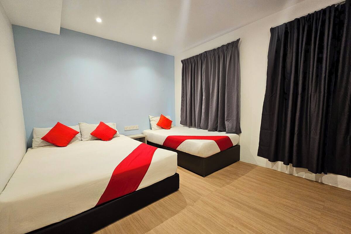 A hotel room with two beds, a blue wall, a black curtain, and a wooden floor.