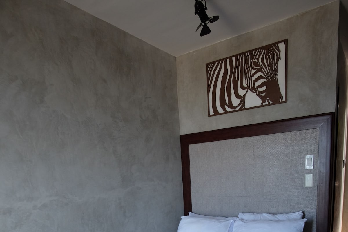 A neatly made bed with white linens and a zebra-themed wall decoration.