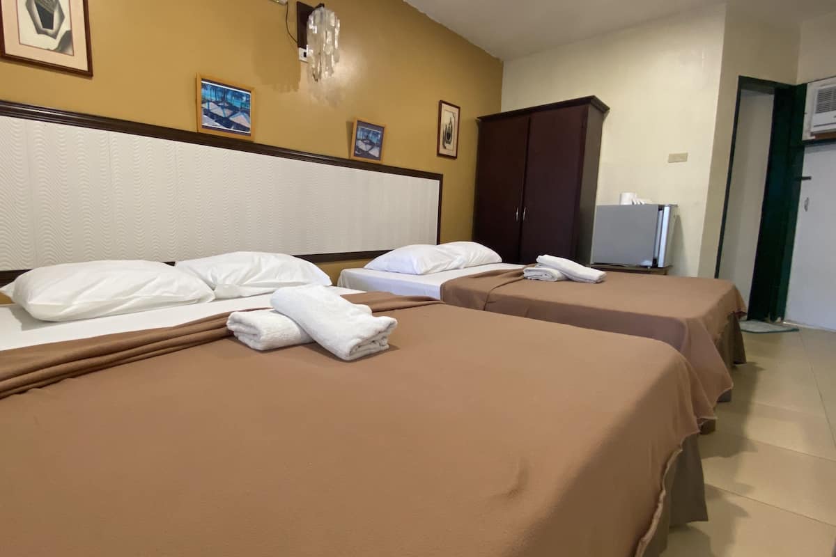 A hotel room with two beds, each with a brown bedspread and white pillows. There are framed pictures on the wall above the beds.