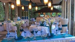 A banquet hall with round tables covered in white tablecloths, blue centerpieces, and white chairs with blue sashes.