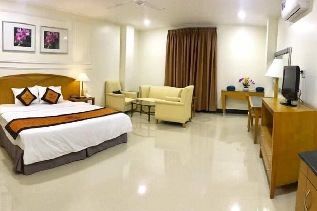 A hotel room with a bed, a desk, a chair, a sofa, and a television.