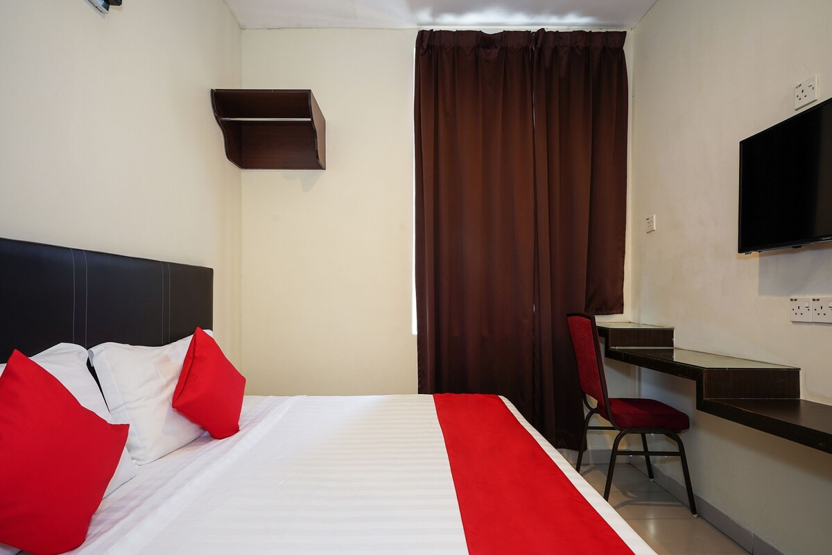 A hotel room with a bed, a desk, a chair, a TV, and a window with curtains.